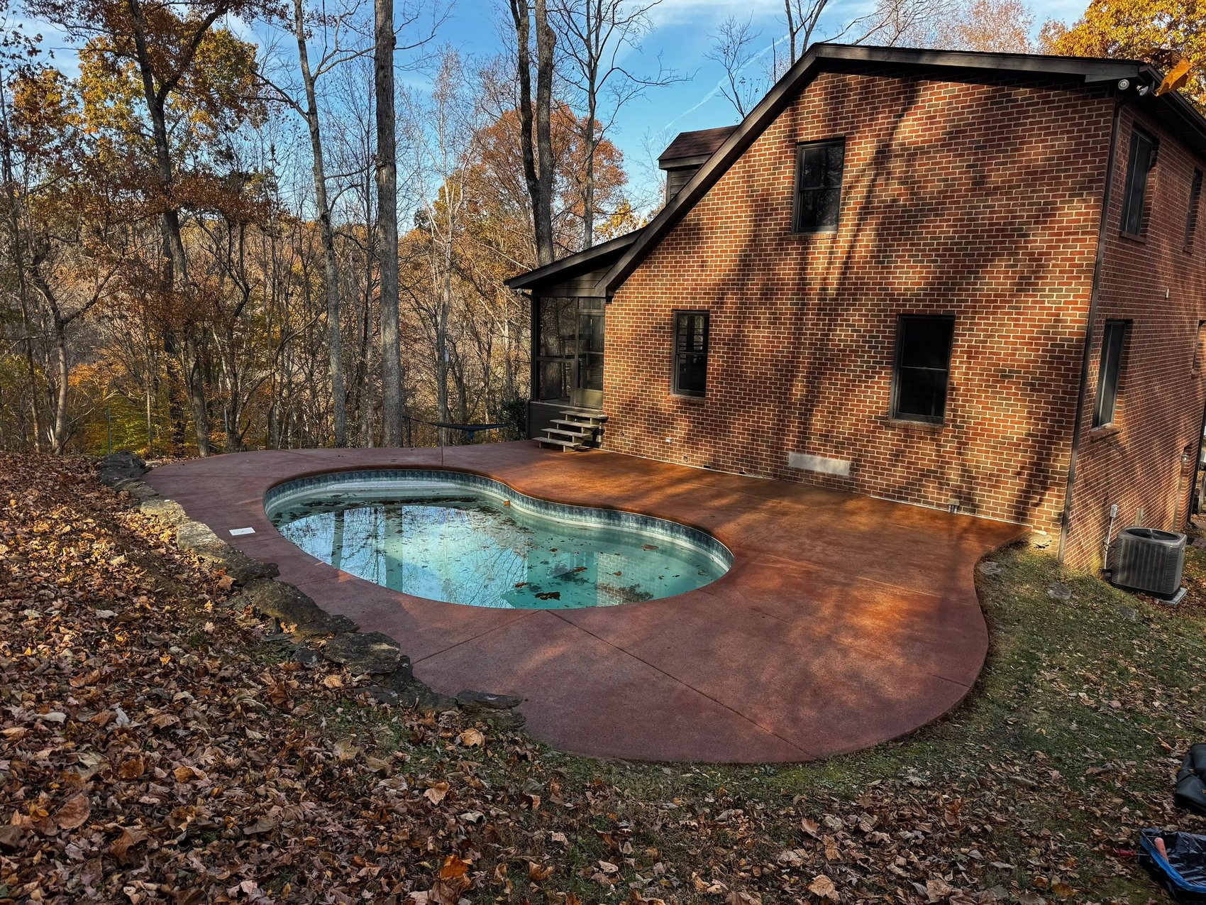 Freeform pool and spa with a natural boulder waterfall, surrounded by a warm stained-and-sealed concrete deck in Ashland City