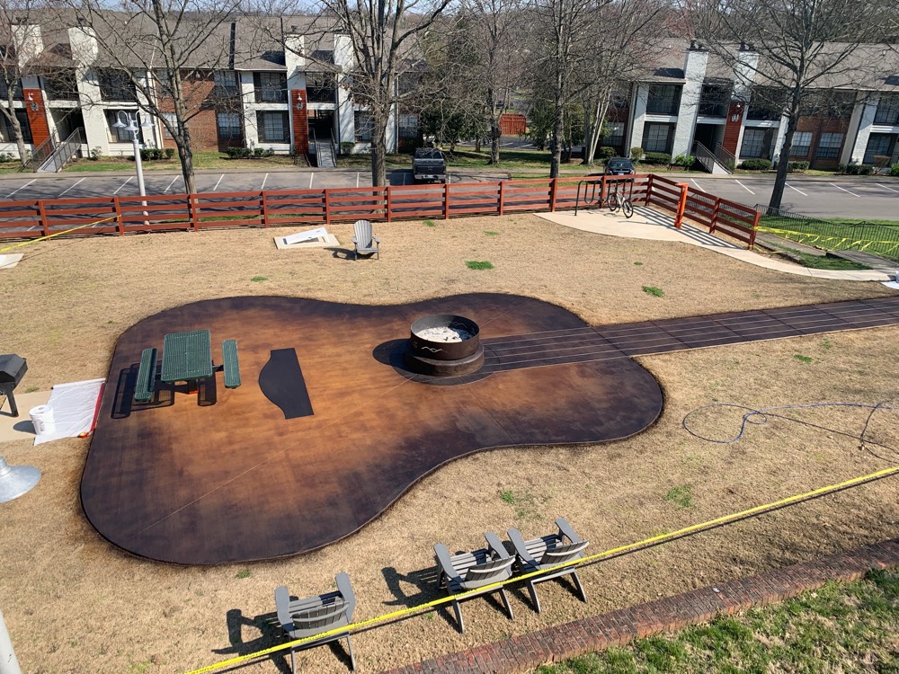 Guitar-shaped fire pit patio in Nashville stained a deep mottled walnut, with the strings and fretboard worked into the surface